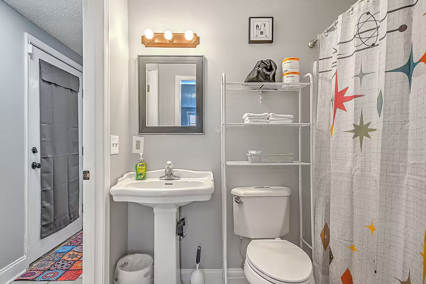 A bathroom with a sink, mirror, toilet, and shelves with towels.