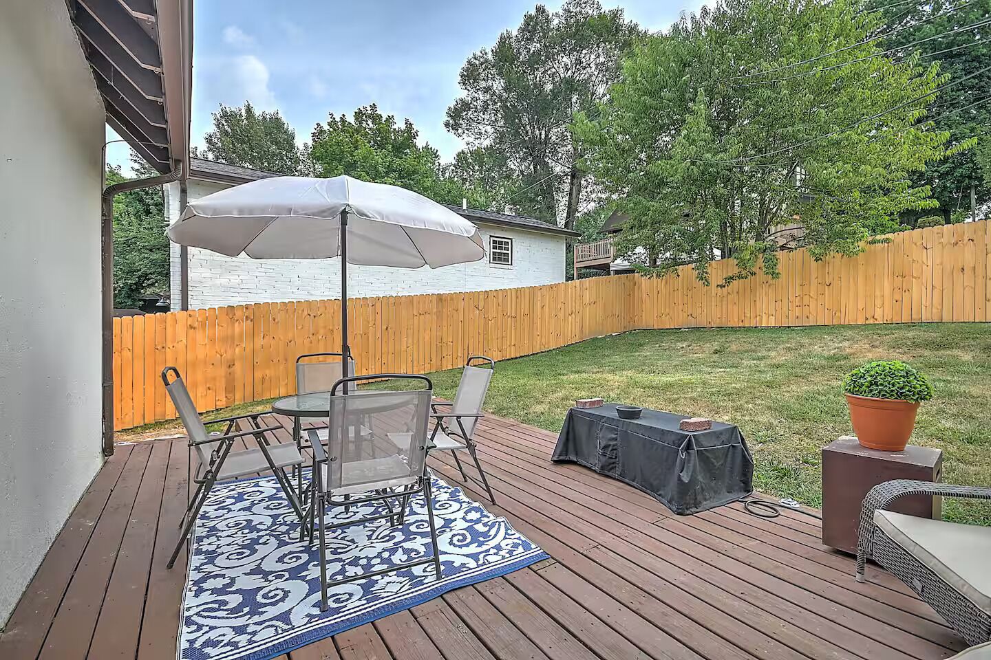 A deck with a table and chairs, a covered umbrella, and a potted plant.