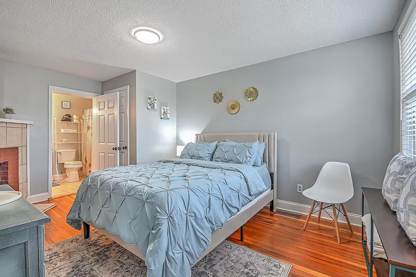 A bedroom with a bed, a chair, a desk, and a window.