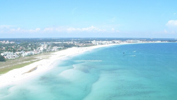 Paisagem urbana costeira com uma praia arenosa extensa e mar azul cristalino.