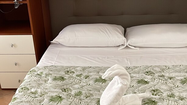 A neatly made bed with a tropical leaf pattern bedspread, a folded white towel, and a white pillow. - Da Colomba city center (Bergamo)