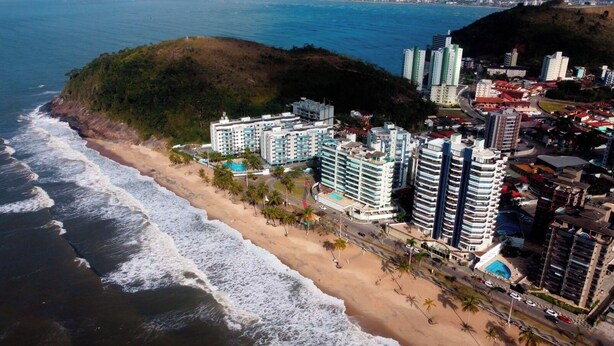 A coastal hotel with multiple high-rise buildings, a beach, and a hilly backdrop.