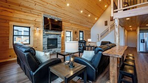 Un salon chaleureux avec une cheminée, des canapés en cuir, une table basse en bois et un coin bar avec des tabourets.