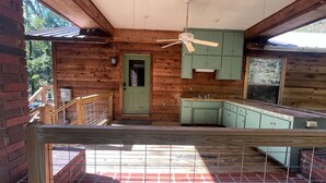 Une cabane en bois avec un coin cuisine, une porte verte et un ventilateur de plafond.