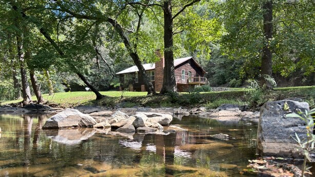 Une cabane entourée d’un paysage naturel, avec un étang et des rochers.