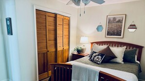 Une chambre à coucher avec un lit en bois, une table de chevet, une lampe, un tableau encadré et une armoire aux portes coulissantes.