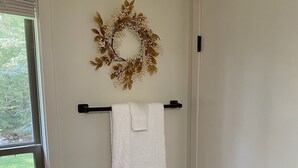 Une salle de bain avec une serviette blanche suspendue à une barre à serviettes noire, une guirlande décorative accrochée au mur et une fenêtre avec des stores.