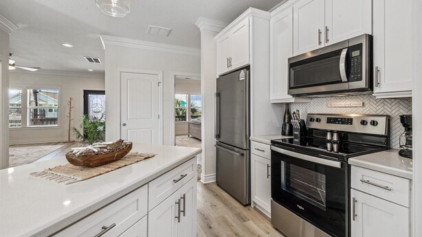 A modern kitchen with white cabinetry, stainless steel appliances, and a large island with a bowl. - After Dune Delight Pointe San Luis far West End (Galveston)