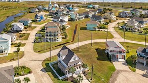 An aerial view of a coastal residential area with houses, a water tower, and a beach in the background. - After Dune Delight Pointe San Luis far West End (Galveston)