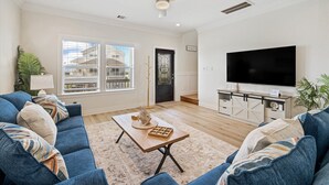A living room with a blue sofa, a wooden coffee table, a flat-screen TV, and a ceiling fan. - After Dune Delight Pointe San Luis far West End (Galveston)