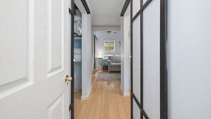 Un corridoio con pavimento in legno che conduce a una camera da letto con un letto, un comodino e una finestra.