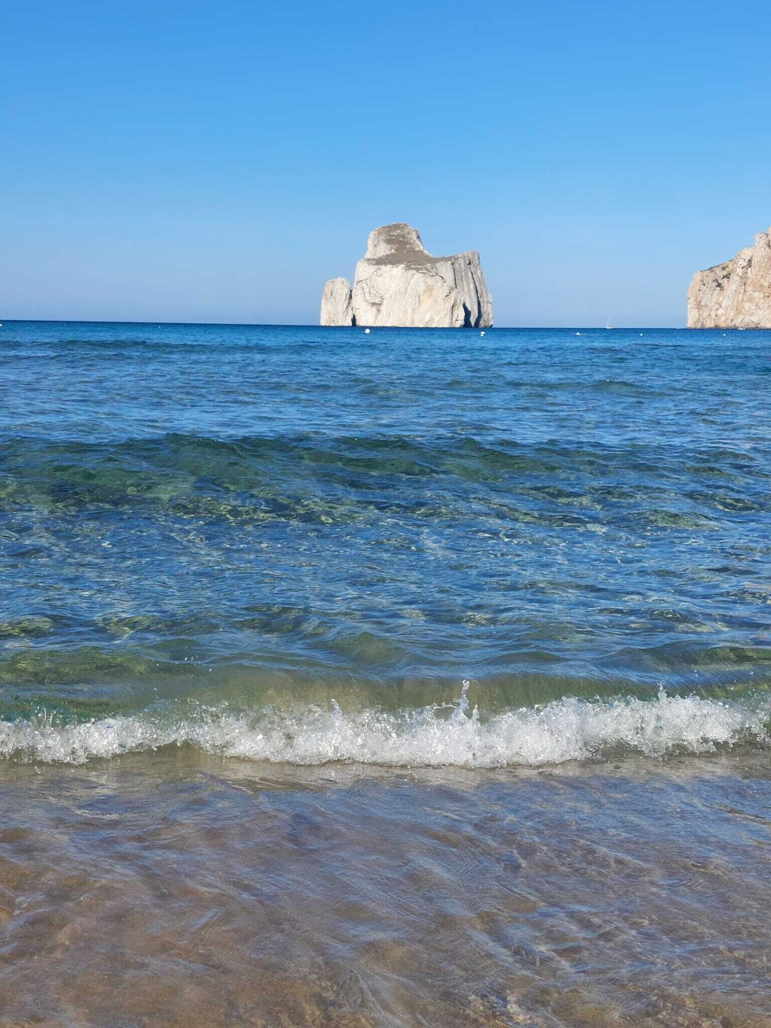 A clear view of a beach with calm waters and two prominent rock formations in the distance.