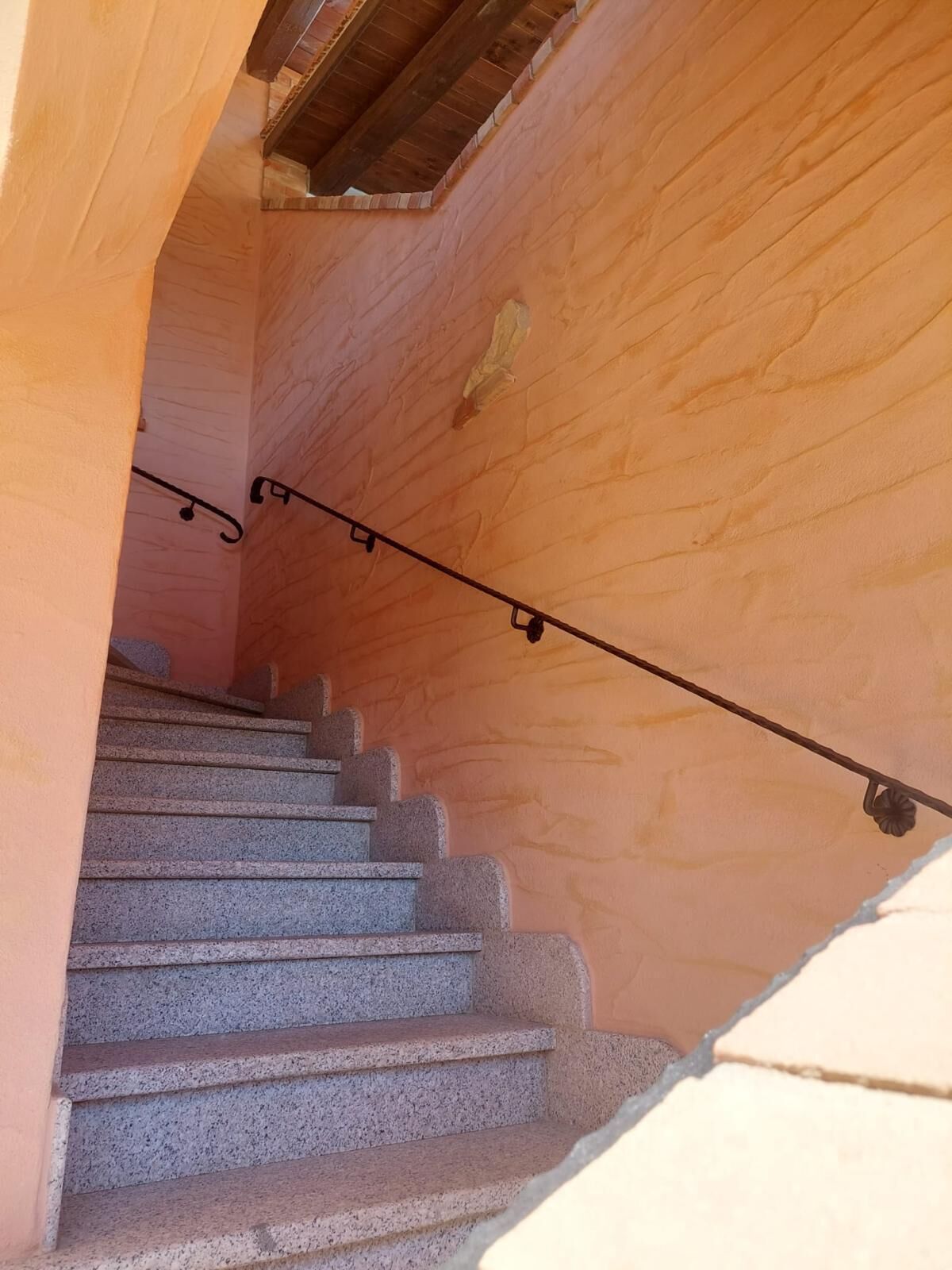 Una escalera de piedra con barandilla de madera que baja a un nivel inferior.