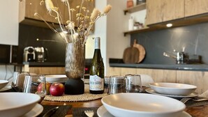 Une table à manger dressée avec de l’assiette blanche, une bouteille de vin et un vase contenant des fleurs séchées.