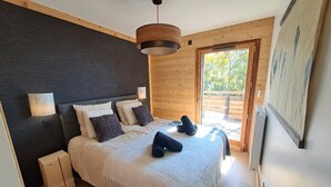 Une chambre à coucher avec un lit, des tables de chevet, un luminaire suspendu et une vue sur l’extérieur.