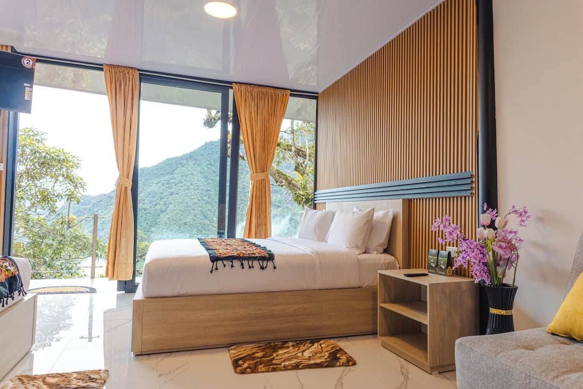 Une chambre moderne avec un grand lit, une tête de lit en bois et une vue sur un paysage montagneux grâce à de grandes fenêtres.