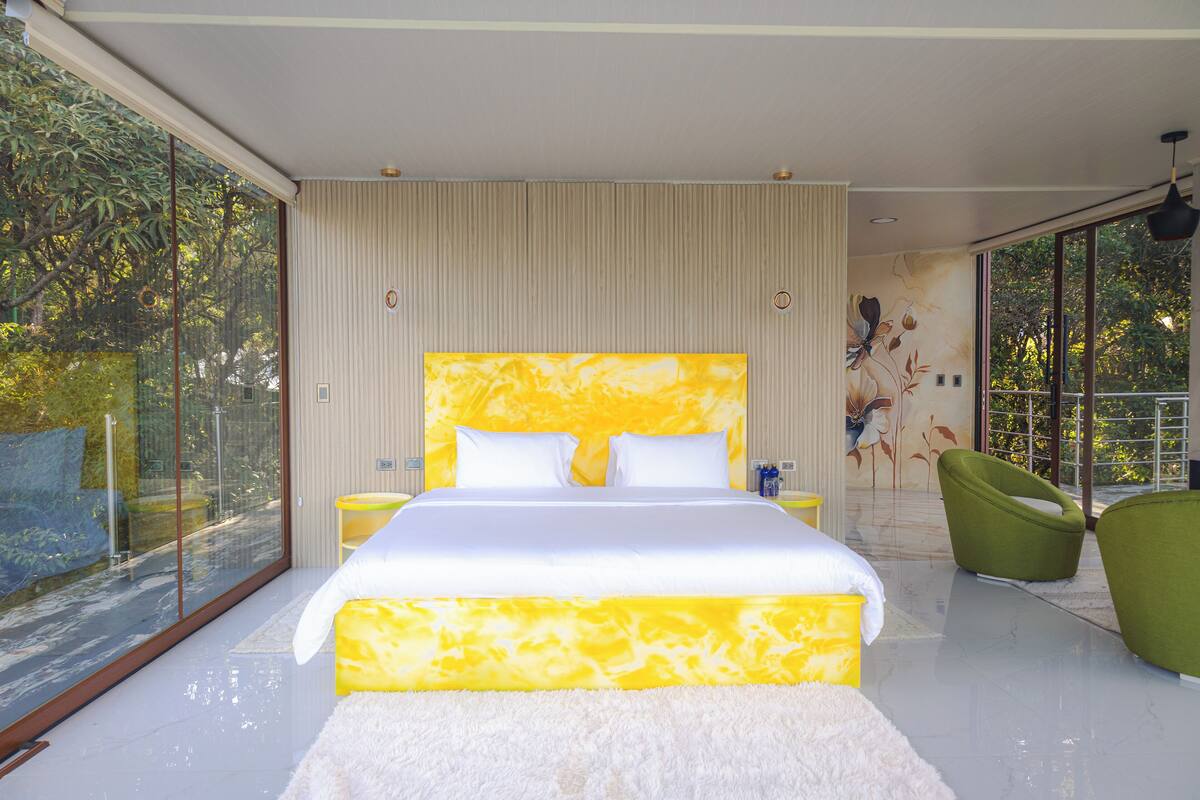 Ein modernes Schlafzimmer mit einem großen Bett, einem grünen Sessel und Blick durch große Glasfenster.