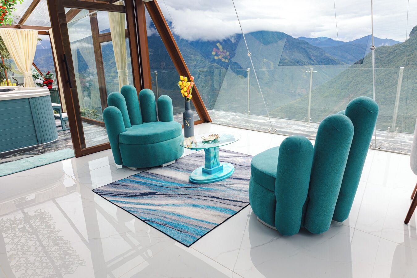 Una habitació moderna amb cadires tapissades de color blau verd, una taula de centre de vidre i vista a les muntanyes a través de grans finestres.