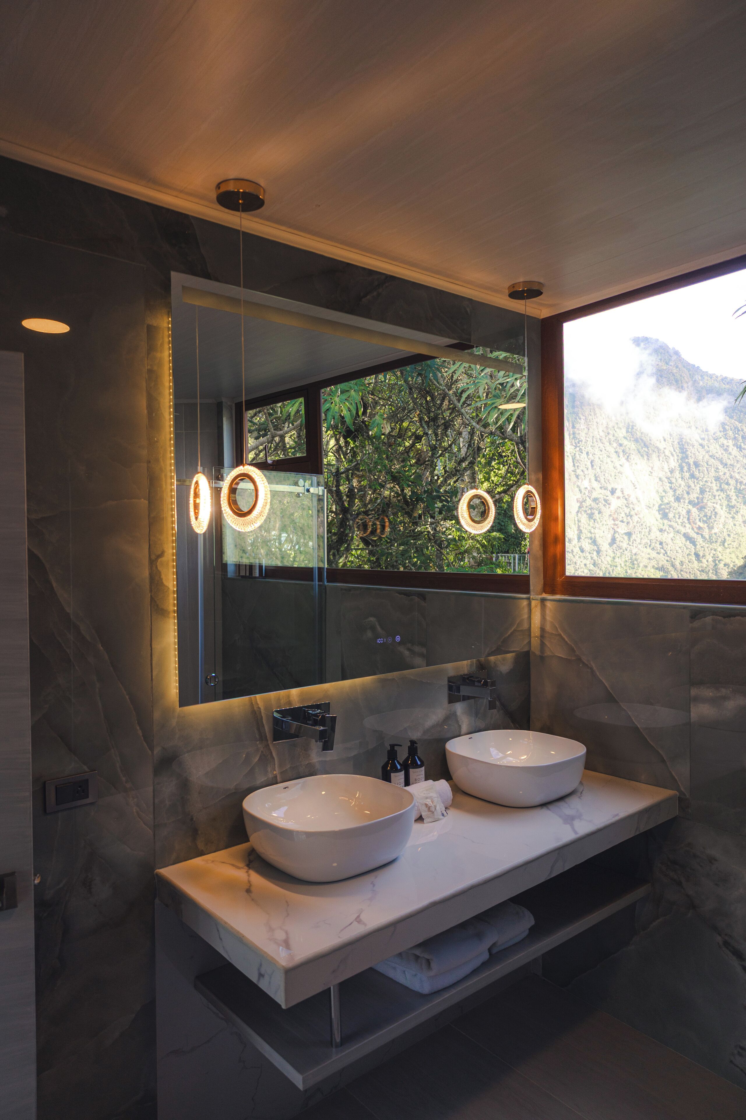 Un baño moderno con dos lavabos, un espejo grande y vistas a un paisaje montañoso.