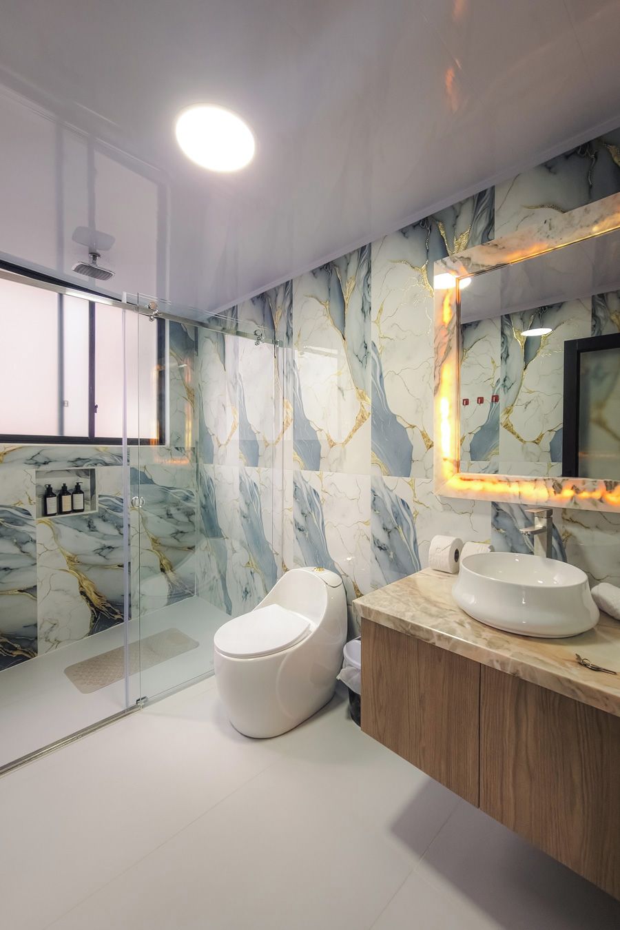 Un baño moderno con ducha de vidrio, salpicadero de mármol y tocador con lavabo.