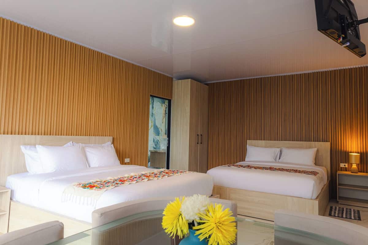 Ein Hotelzimmer mit zwei Betten, Holzwandverkleidung, einem Glastisch und einer Vase mit Blumen.