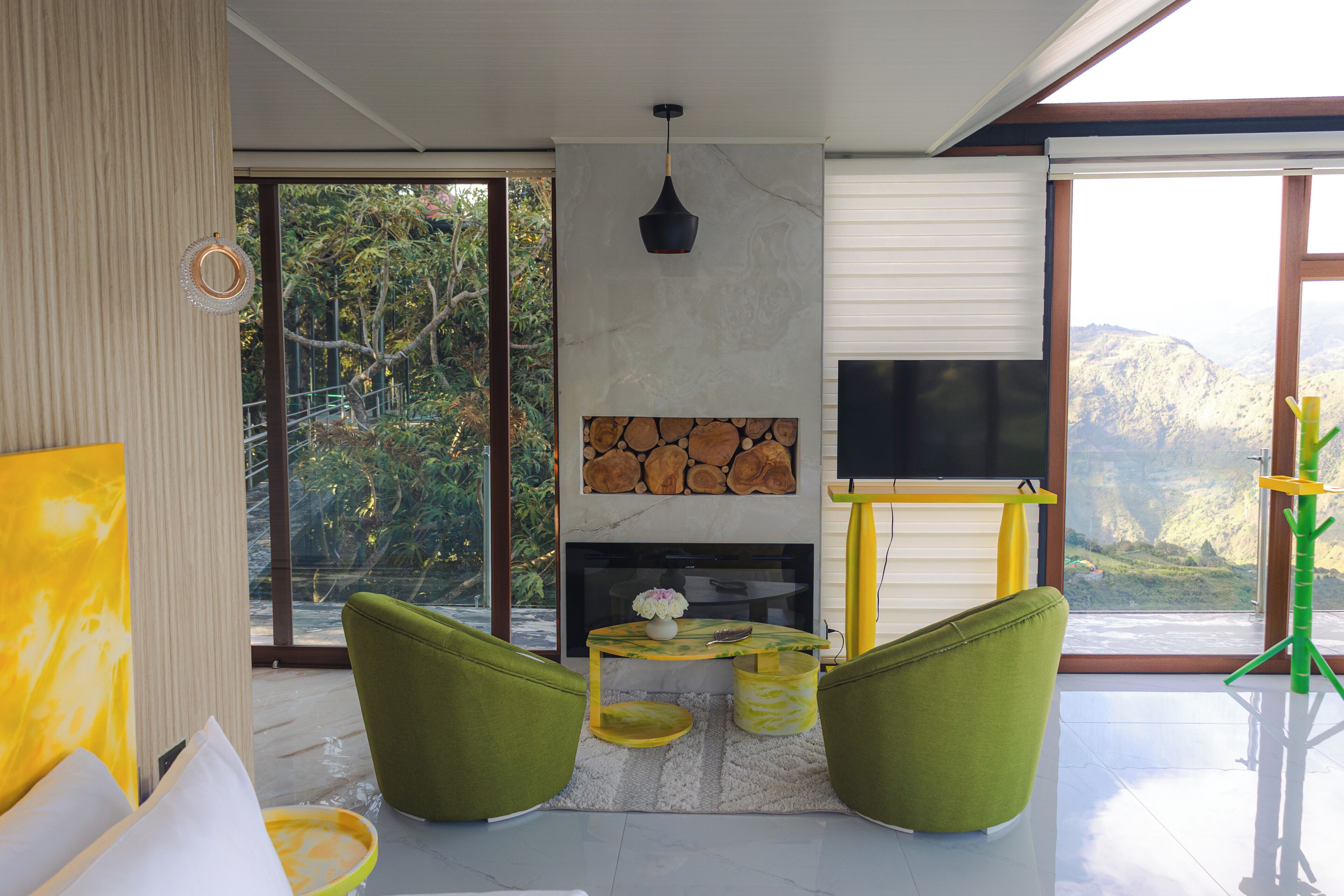 Una sala de estar moderna con chimenea, sillones verdes, televisor y vistas a montañas.
