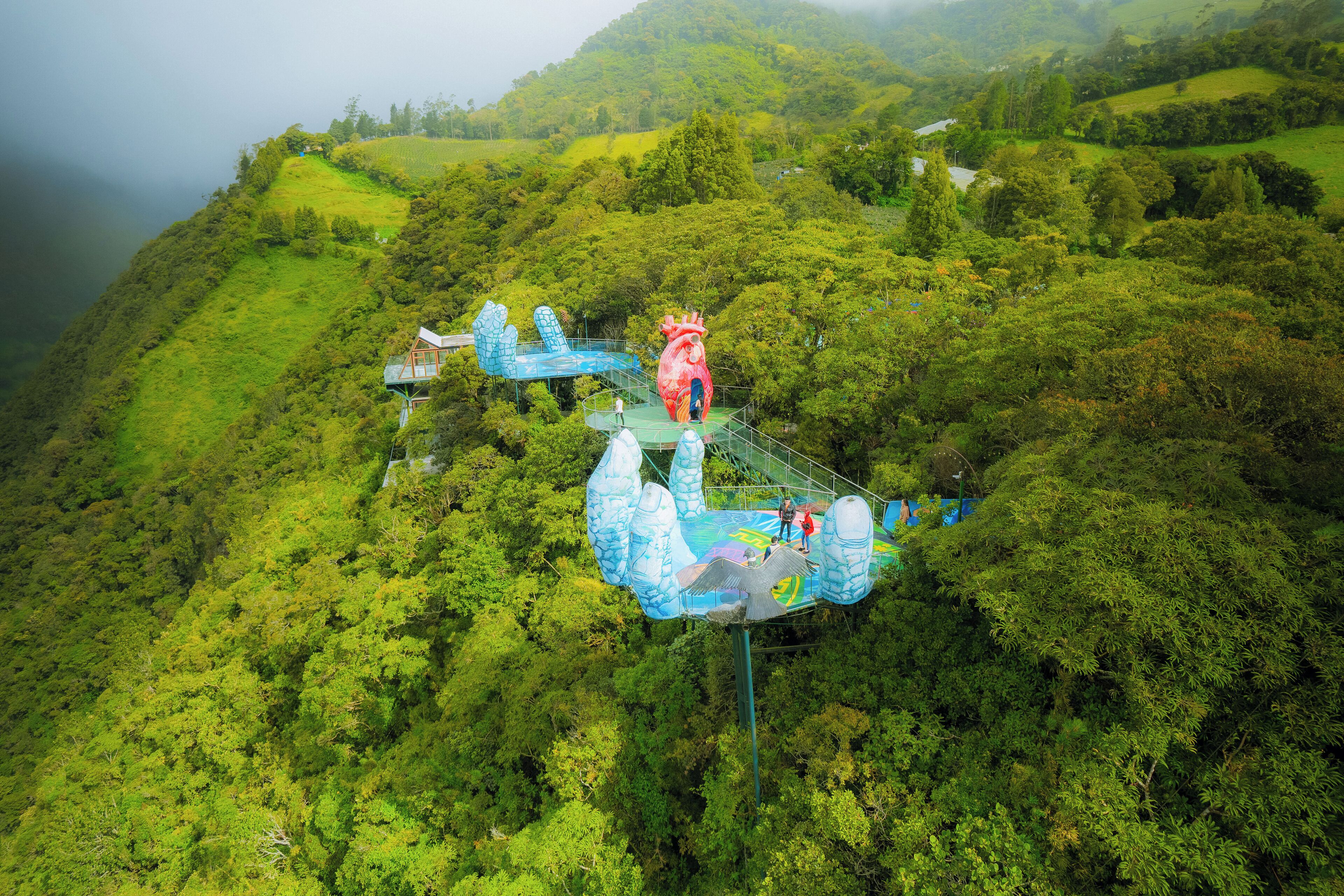 A scenic view of a lush green valley with a large heart-shaped structure and a blue whale sculpture.