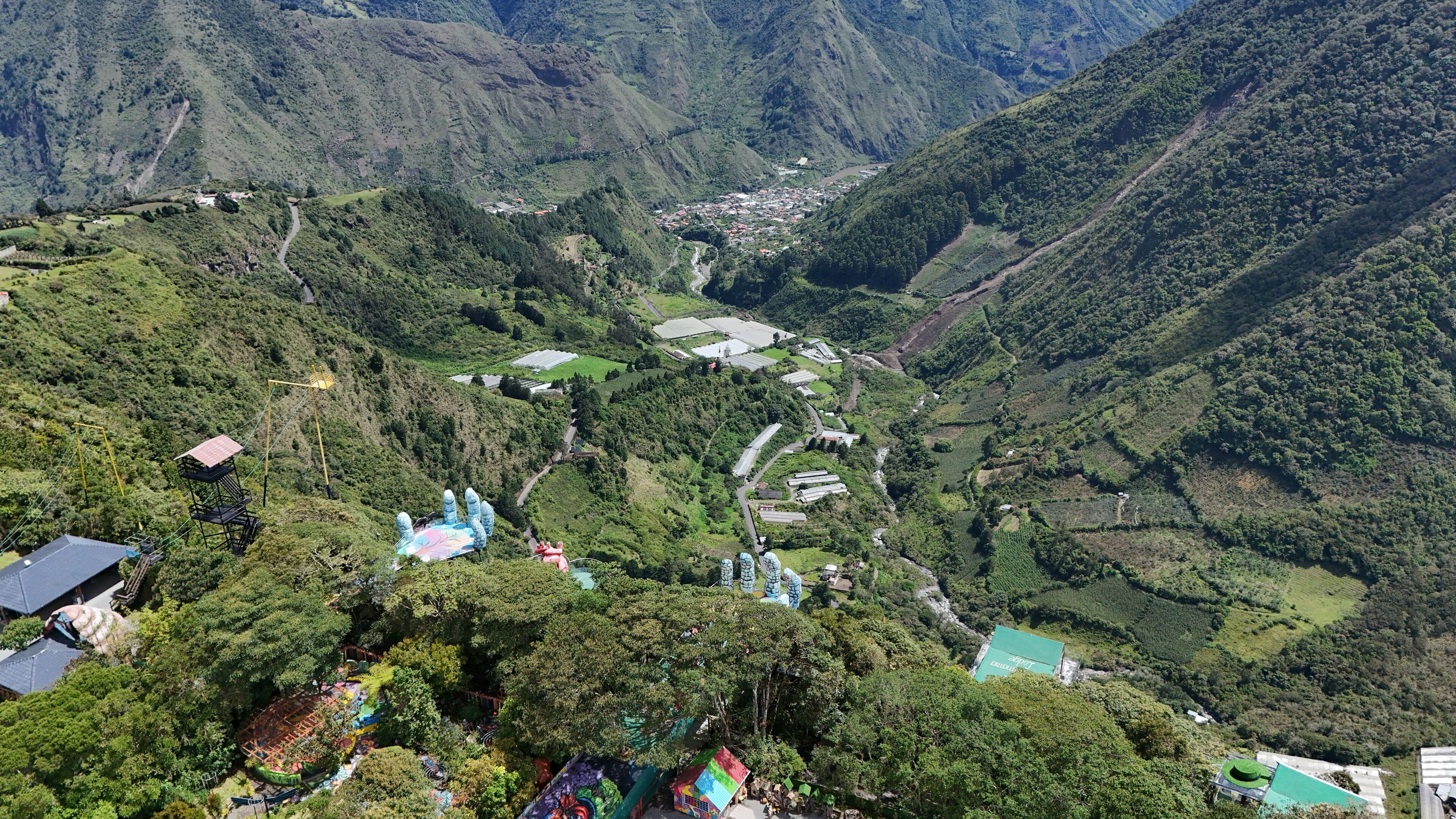A mountainous landscape with a village nestled in a valley. There are several buildings, including a large structure with a green roof and smaller houses with red roofs.