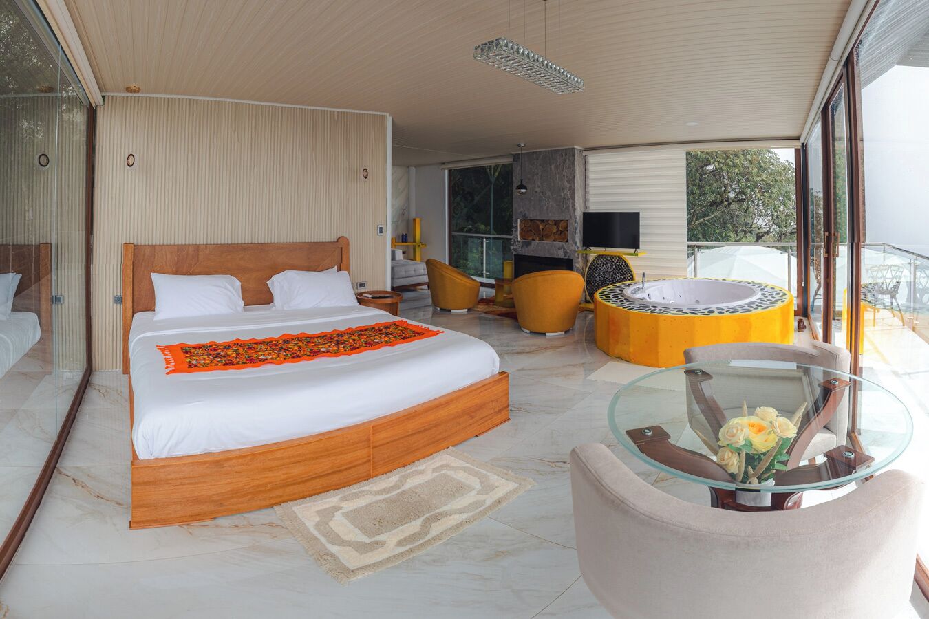 Een moderne slaapkamer met een groot bed, een glazen bijzettafeltje met bloemen, en uitzicht op de omgeving.