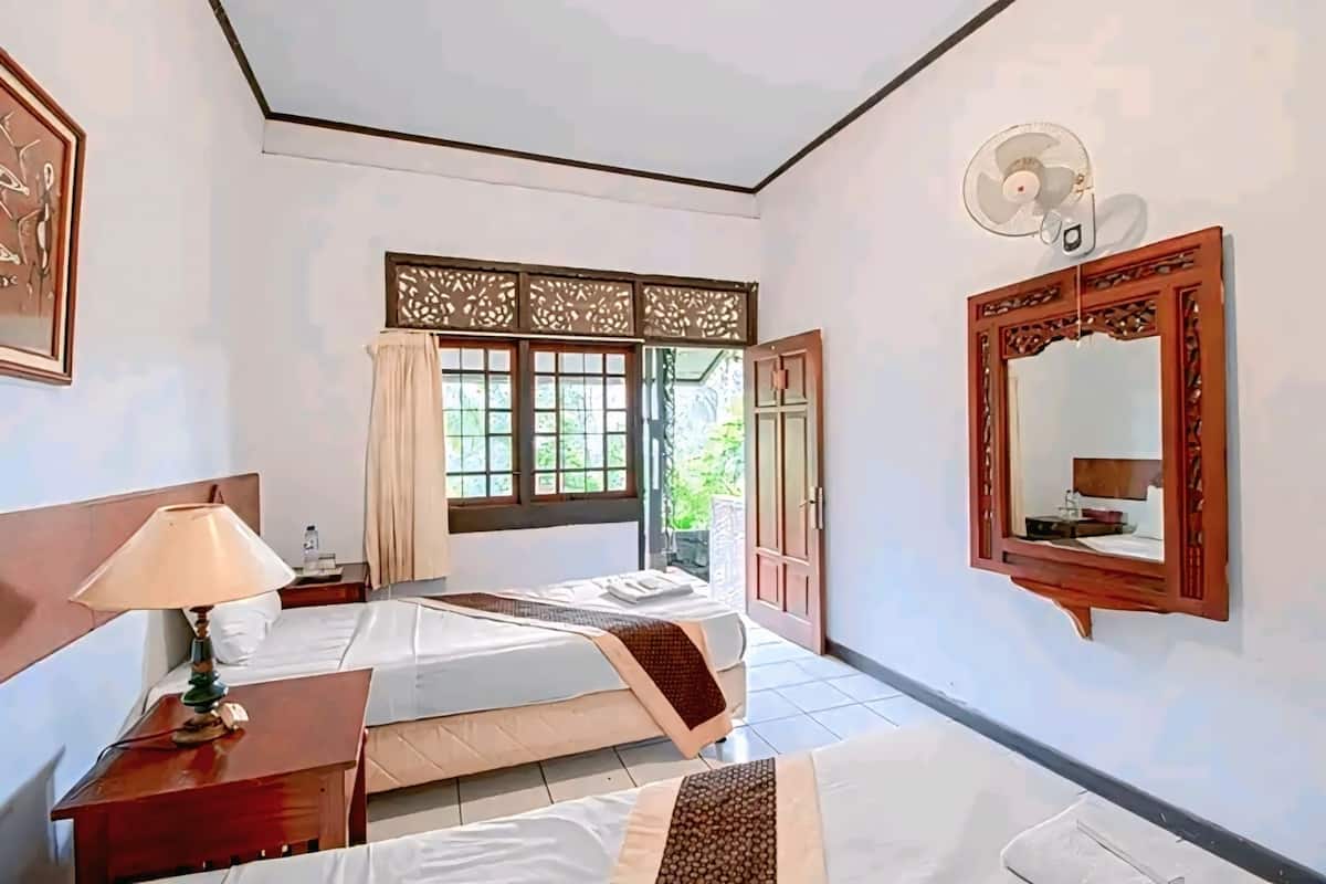 Une chambre d’hôtel avec deux lits, une table de chevet avec une lampe, un grand miroir et une fenêtre donnant sur un paysage verdoyant.