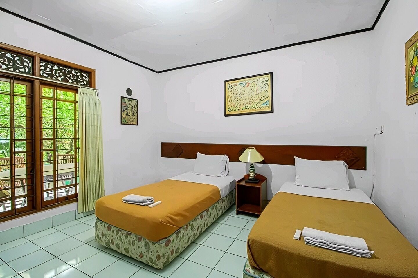 A hotel room with two beds, a window with a view, and a small table with a lamp.