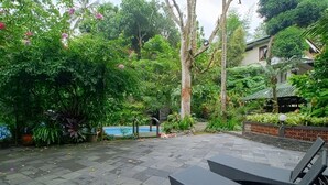 Um pátio com piscina, rodeado por vegetação exuberante e um espaço de estar com piso de azulejos.