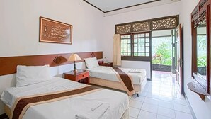Quarto de hotel com três camas, um ventilador de teto, uma janela com vista para vegetação e um painel decorativo na parede.