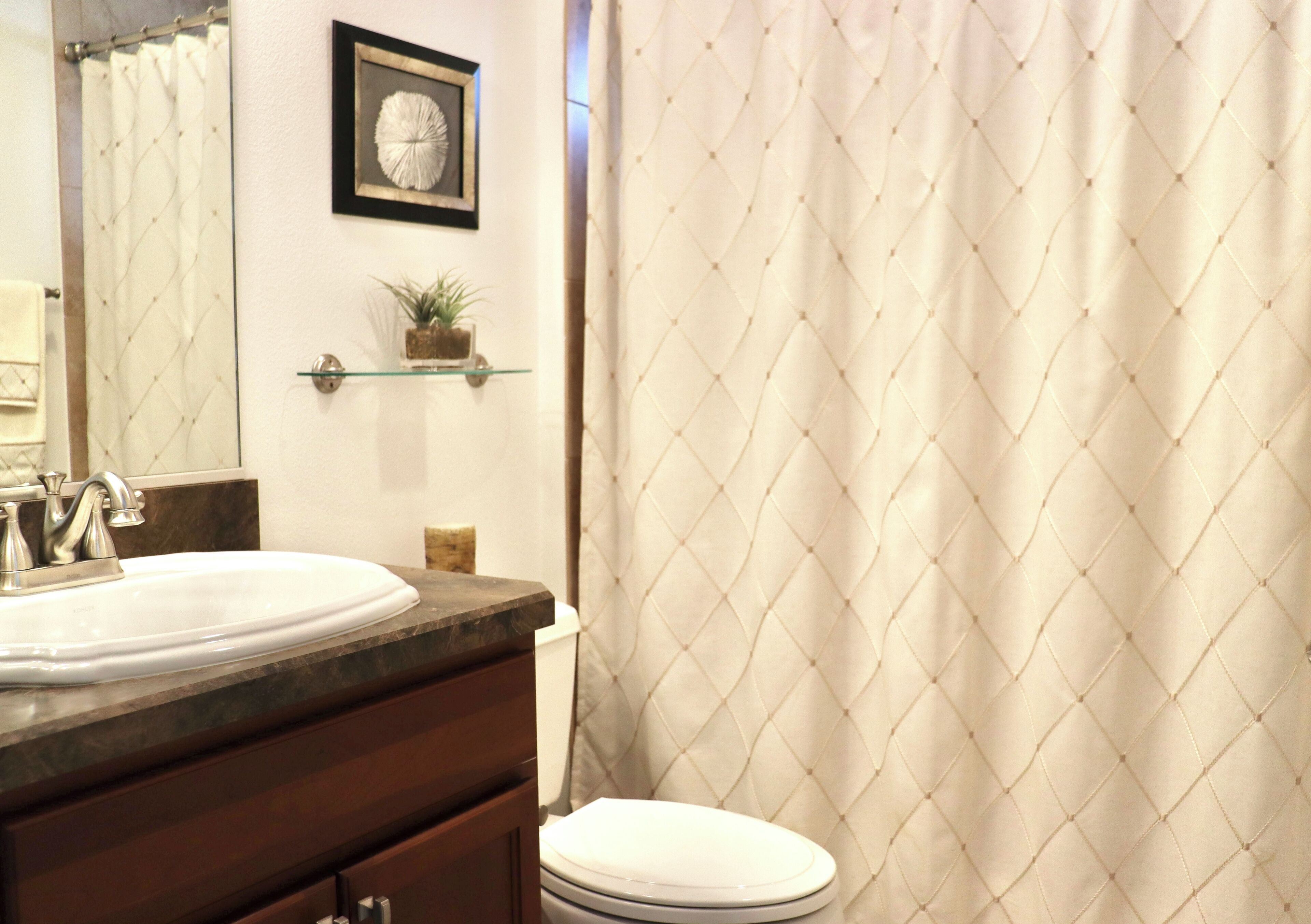 Une salle de bain avec un lavabo blanc, des toilettes, un tableau encadré accroché au mur et une plante en pot posée sur une étagère.