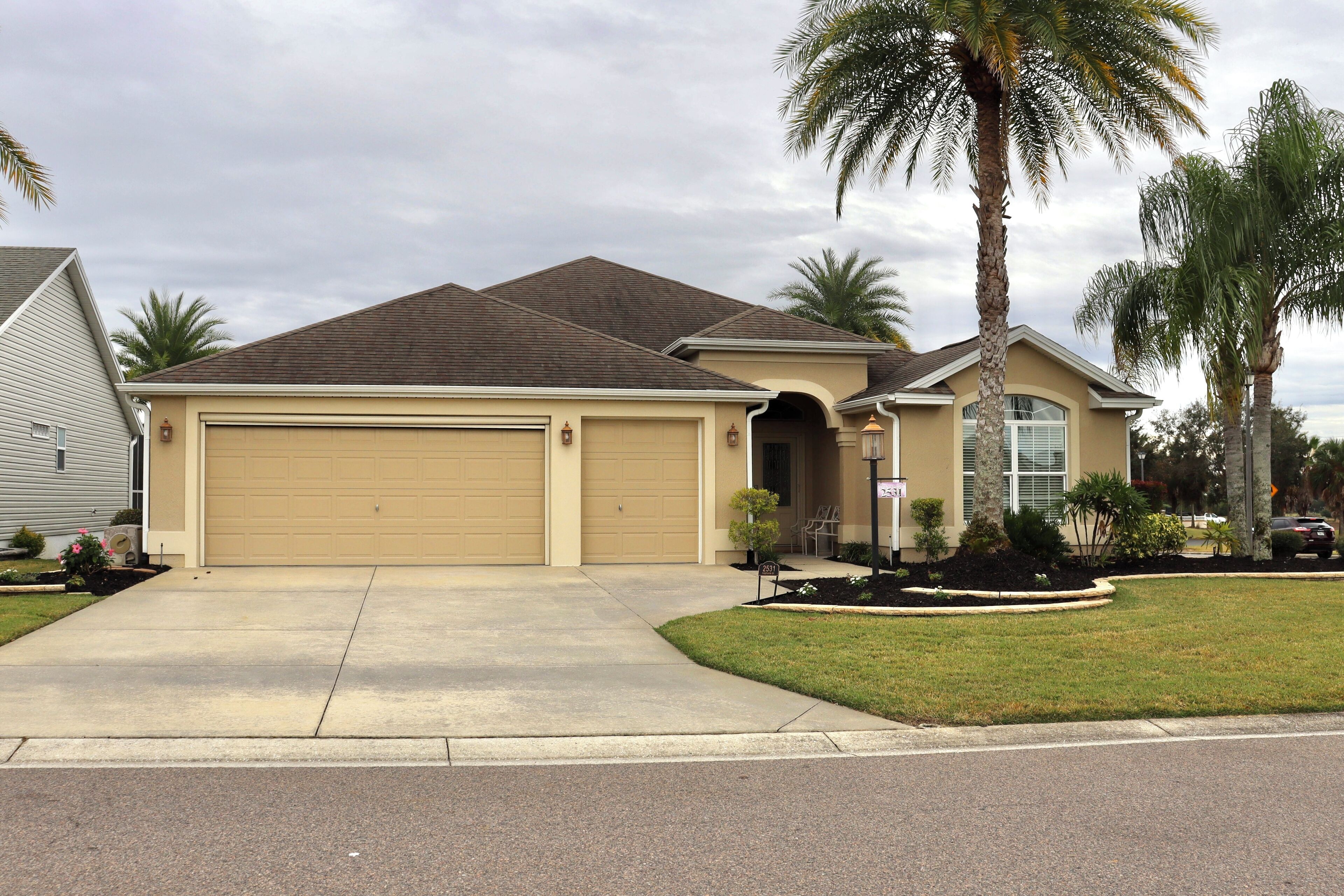 A single-story house with a beige garage, a small front yard with a palm tree, and a driveway leading to the garage.