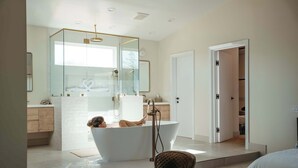 Un baño moderno con una bañera independiente, ducha con cerramiento de vidrio y zona de lavamanos a la vista.
