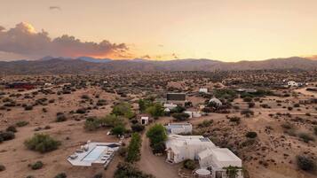 A desert landscape with a cluster of buildings, including a large white structure with a swimming pool and smaller surrounding buildings.