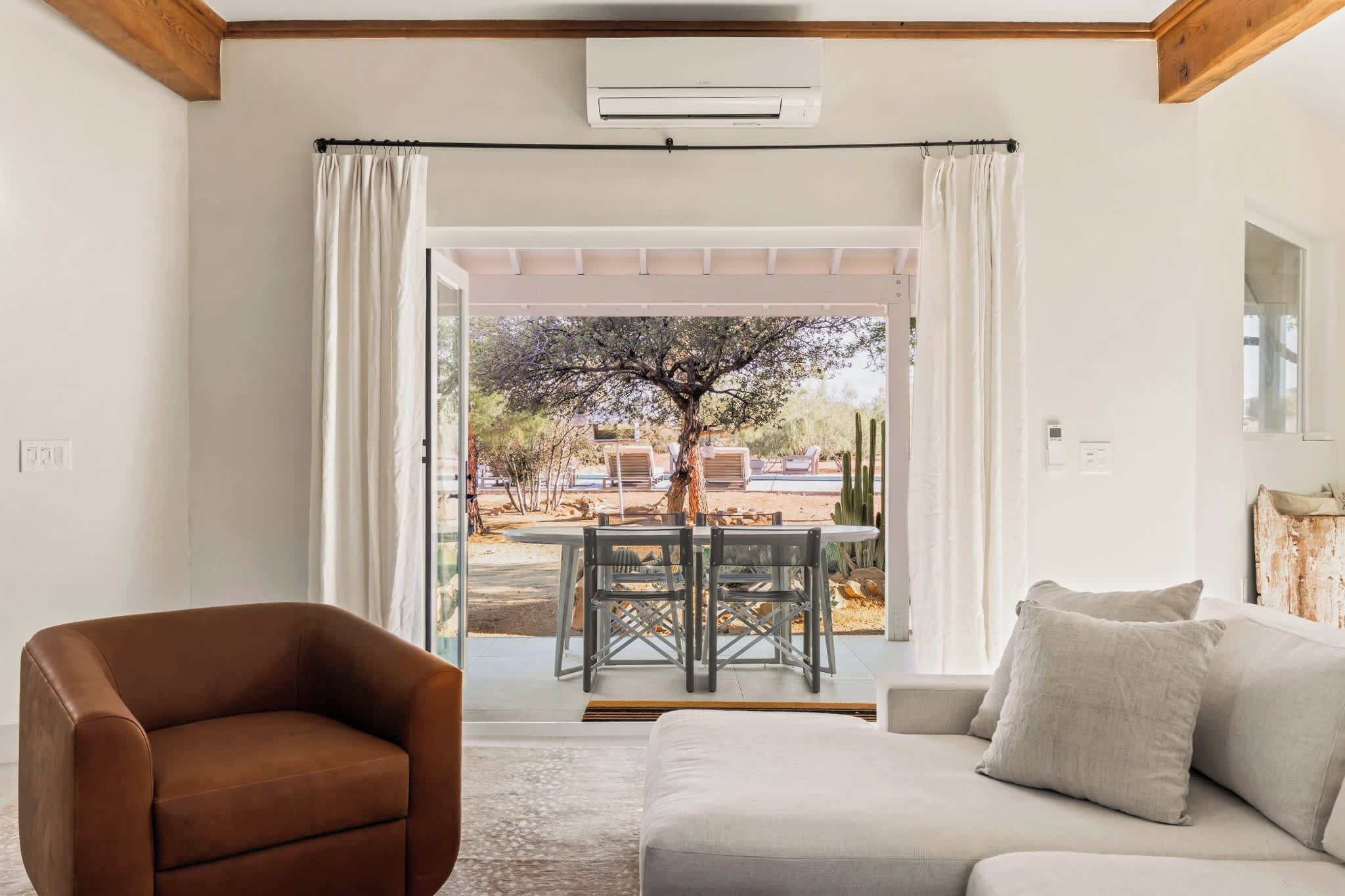 A living room with a brown armchair, a grey sofa, and a glass door leading to an outdoor area with a table and chairs.