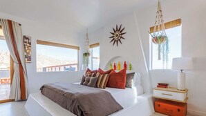 Quarto moderno com uma cama grande, mesa de cabeceira com abajur e vista para o exterior.