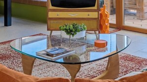 Uma sala de estar com uma televisão antiga, uma mesa de centro de vidro e um sofá de couro.