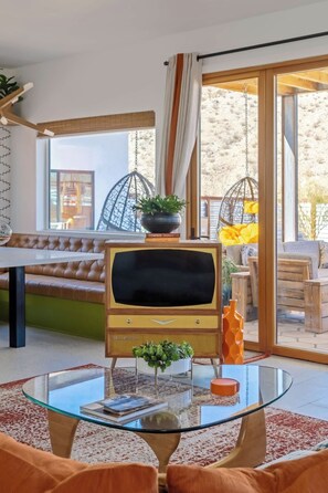 Ein Wohnzimmer mit einem Vintage-Fernseher, einem Glastisch und einem Ledersofa.