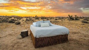 Una cama en un paisaje desértico con vista al atardecer.