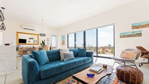 Una sala de estar moderna con un sofá azul, una mesa de centro de madera y un amplio ventanal con vistas al desierto.