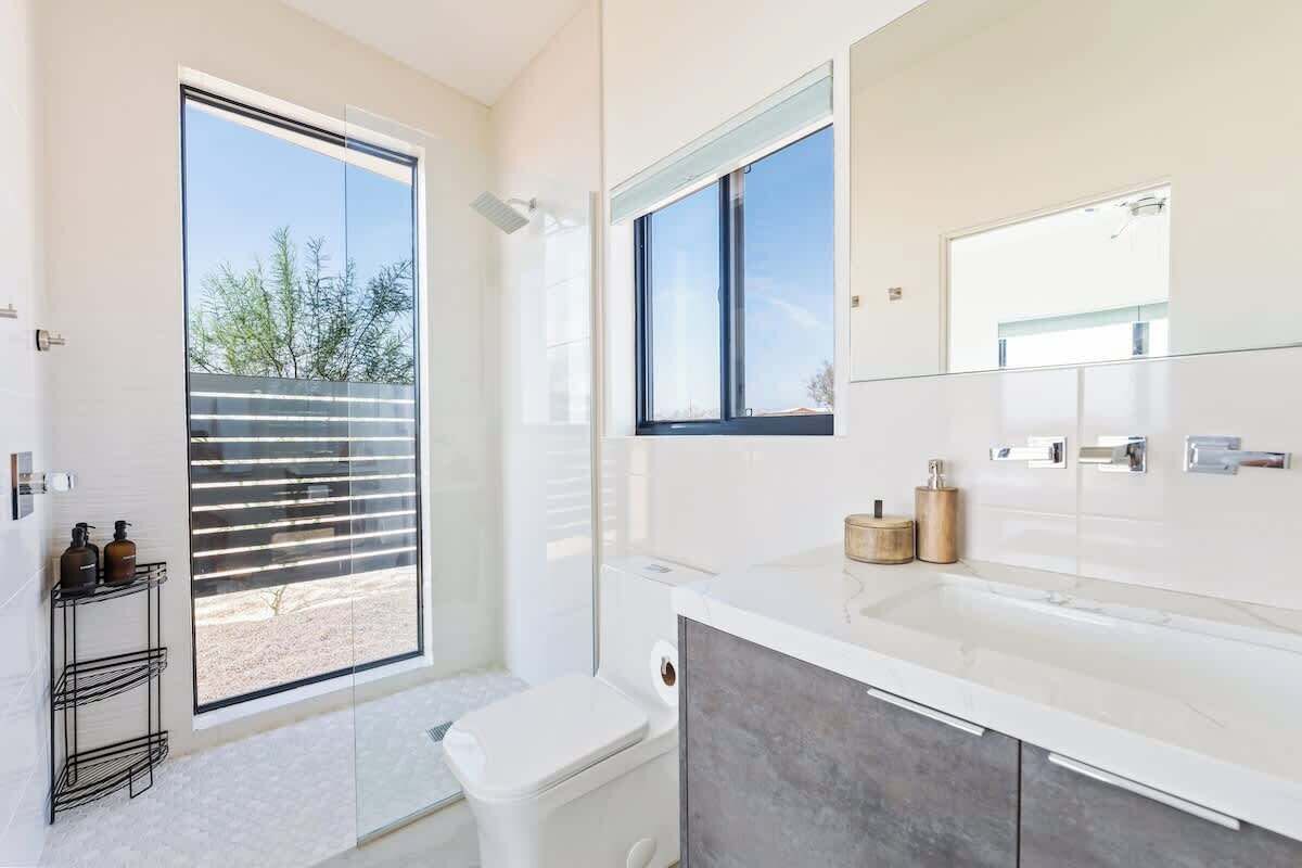 A modern bathroom with a large window, a white sink, and a toilet.