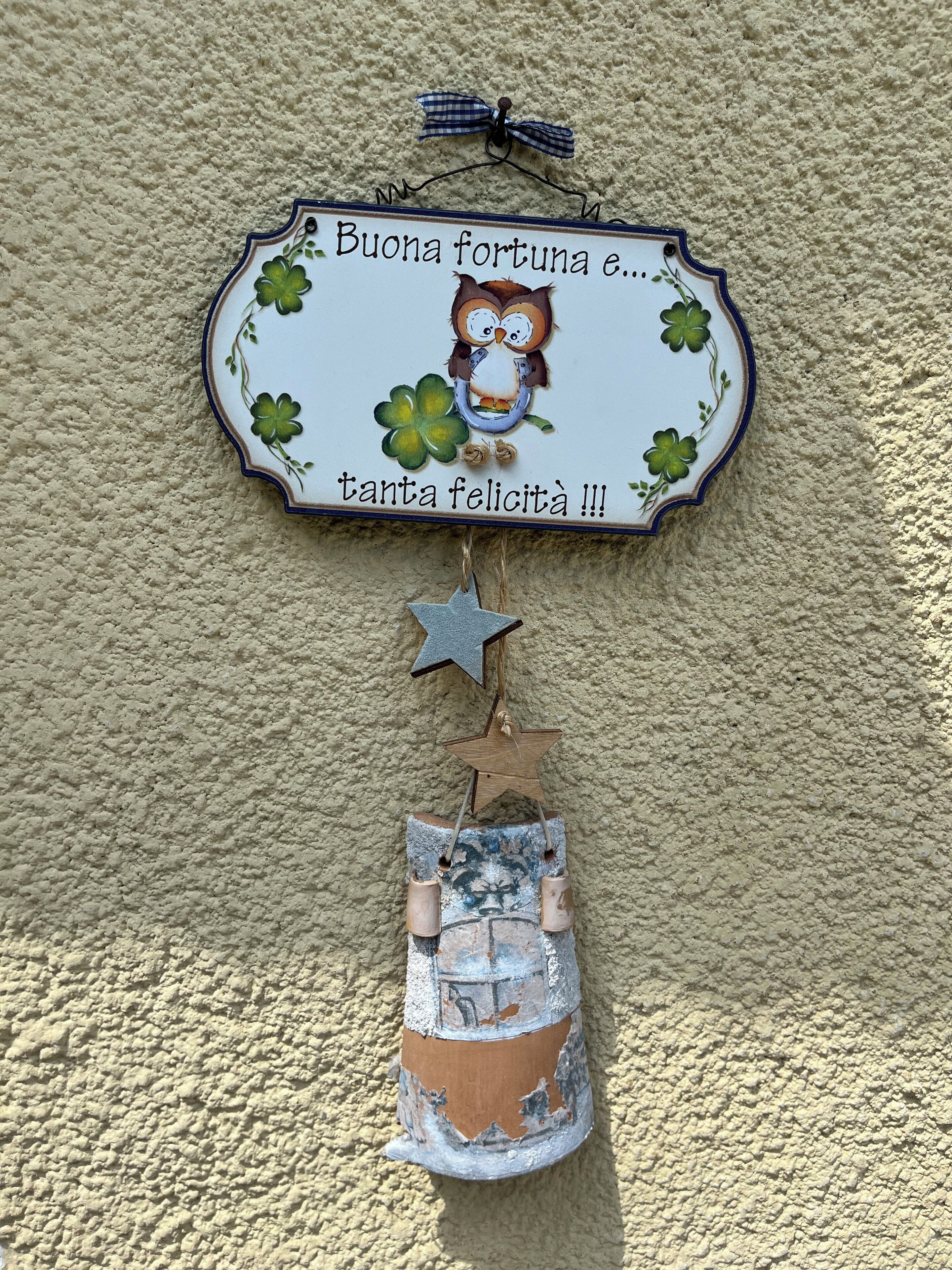 Ein dekoratives Schild mit einem Kleeblatt und einer Eule, an einer strukturierten Wand befestigt.