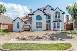 A two-story house with a central arched entrance, a front porch, and a landscaped front yard. - Luxurious Pool Oasis  PS5 
5BR 4 BA Aquarium (Richardson)