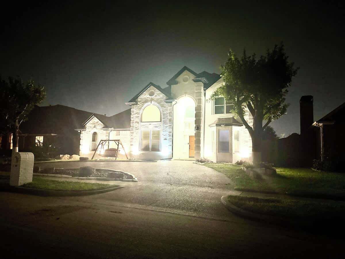Une maison d’habitation la nuit, avec une entrée bien éclairée, une allée et une pelouse.