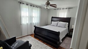 A bedroom with a bed, a ceiling fan, a nightstand, and a chair.