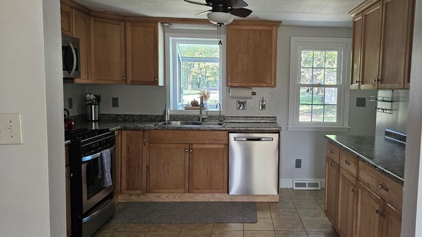 A kitchen with wooden cabinets, stainless steel appliances, a dishwasher, and a window providing a view of the outdoors.