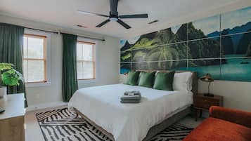 A bedroom with a bed, a ceiling fan, a nightstand, a lamp, a painting, and a window with curtains.